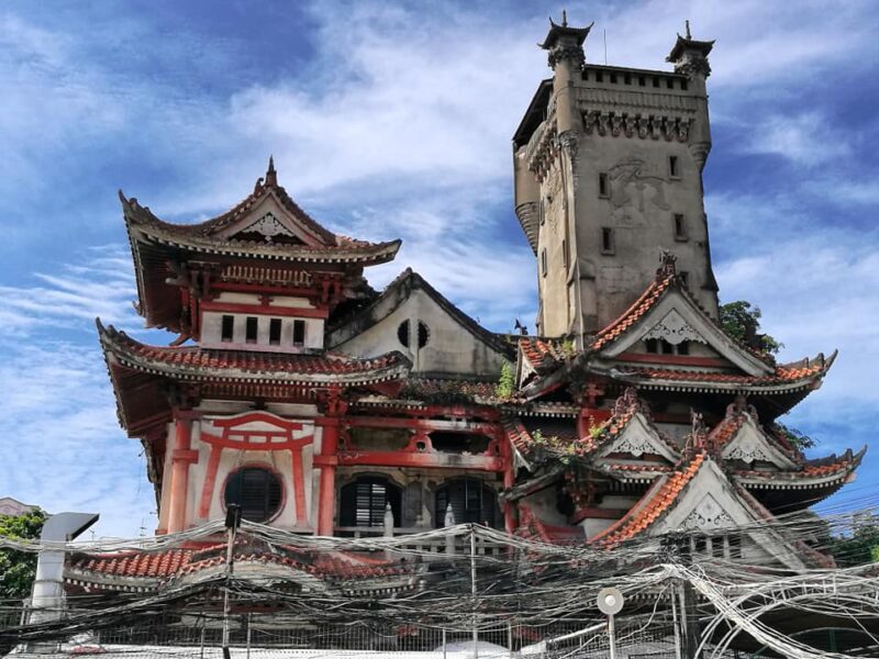 Unique abandoned building with traditional Japanese-style architecture, intricate roof designs, and a tall tower under a bright blue sky.