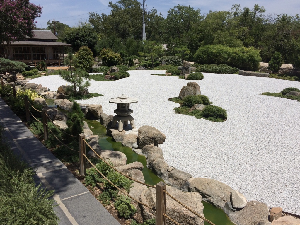 Serene Japanese garden featuring a zen gravel landscape, stone lantern, and lush greenery, creating a tranquil atmosphere.