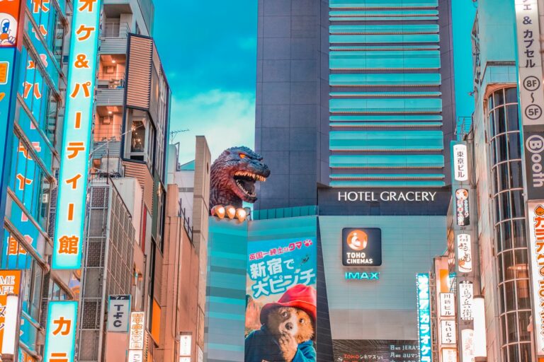 Godzilla head peeking from Hotel Gracery in Shinjuku, Tokyo surrounded by neon signage and billboards.